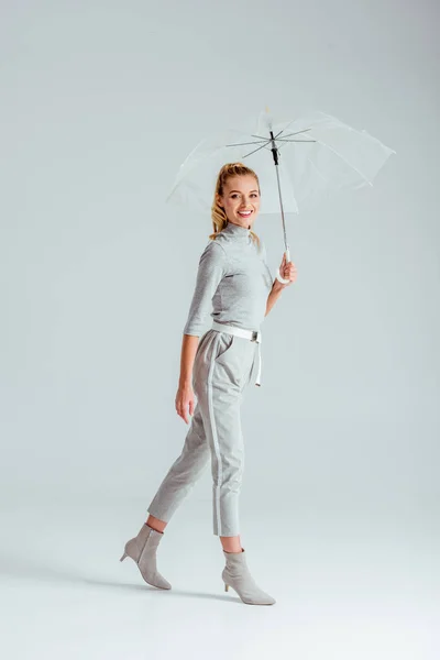 Woman in grey clothes looking at camera and posing with transparent umbrella on grey background — Stock Photo