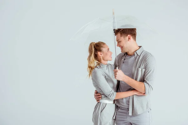 Schönes Paar, das sich anschaut und unter transparentem Regenschirm posiert, isoliert auf grau — Stockfoto