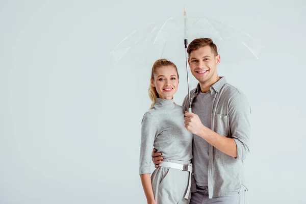 Bella coppia felice guardando la fotocamera e posa sotto ombrello trasparente isolato su grigio — Foto stock