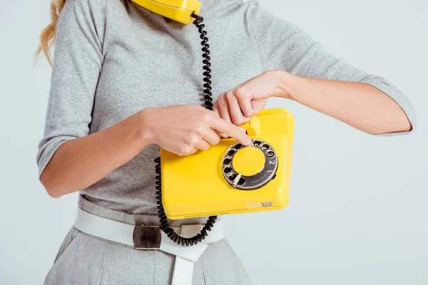 Vista recortada del número de teléfono de marcación de mujer en el teléfono amarillo vintage aislado en gris - foto de stock