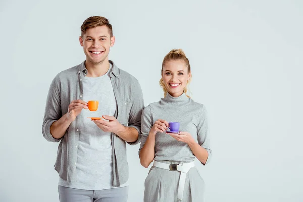 Smiling couple holding coffee cups and looking at camera isolated on grey — Stock Photo