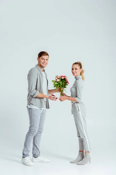 Чоловік вітає жінку з листівкою Валентина і квітковим букетом на сірому фоні — стокове фото