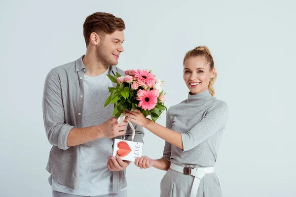 Hombre saludo hermosa mujer con tarjeta de San Valentín y ramo de flores aislado en gris - foto de stock