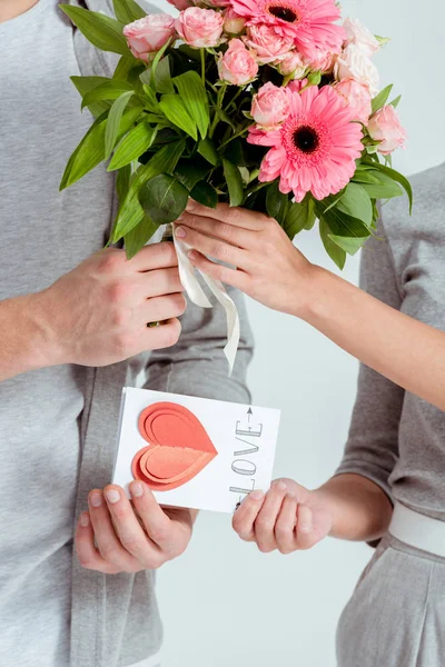 Vista parcial del saludo del hombre mujer con tarjeta de San Valentín y ramo de flores aislado en gris - foto de stock