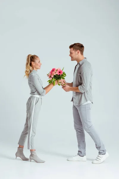 Uomo sorridente dando mazzo di fiori rosa alla donna isolata su sfondo grigio — Foto stock