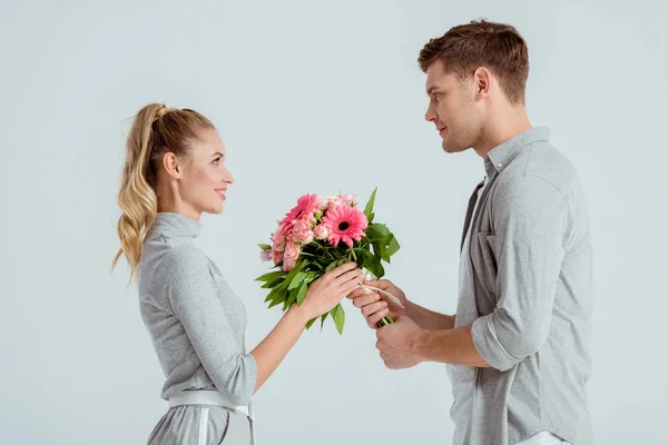 Handsome man giving pink flower bouquet to woman isolated on grey — Stock Photo