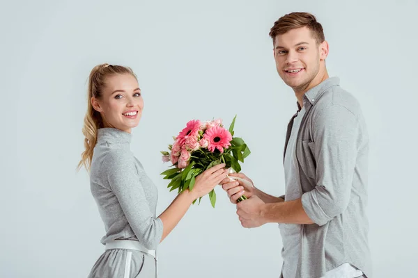 Красивий чоловік дарує квітковий букет красивій усміхненій жінці ізольованій на сірому — стокове фото