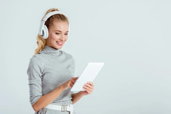 Bella donna in cuffia ascoltare musica e utilizzando tablet digitale isolato su grigio — Foto stock