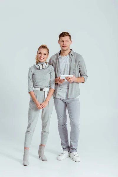 Femme avec écouteurs et homme avec tablette numérique regardant l'appareil photo sur fond gris — Photo de stock