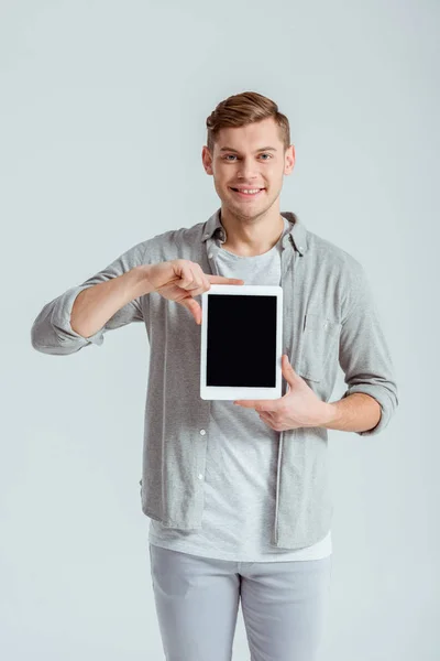 Uomo sorridente in abbigliamento grigio che presenta tablet digitale con schermo bianco isolato su grigio — Foto stock