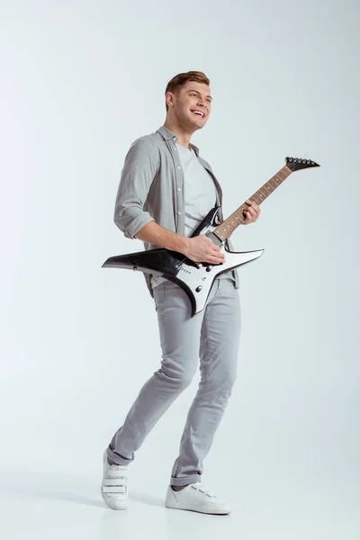 Збуджений усміхнений чоловік у сірому одязі грає на електричній гітарі на сірому фоні — стокове фото