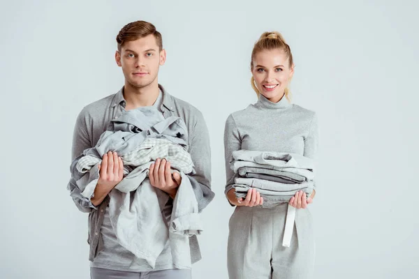 Belo casal olhando para a câmera e segurando roupas cinza isolado no cinza — Fotografia de Stock