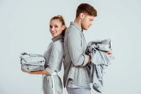 Young couple in grey outfits holding grey clothes isolated on grey — Stock Photo