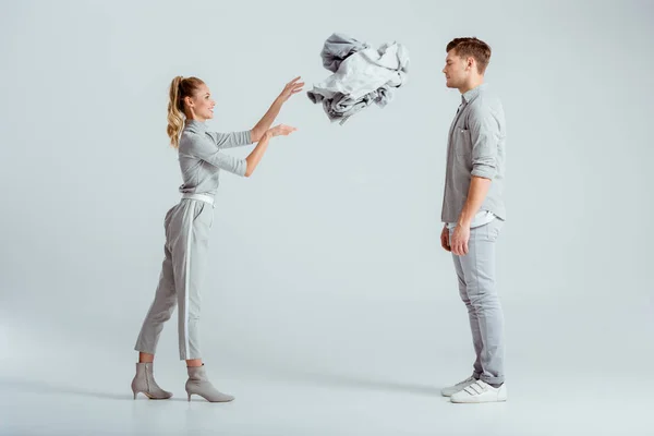 Lächelnde Frau wirft Kleiderstapel auf Mann vor grauem Hintergrund — Stockfoto