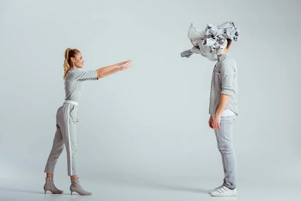 Rubia mujer lanzando pila de ropa al hombre sobre fondo gris - foto de stock