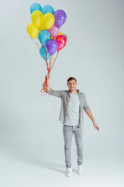 Happy man holding bundle of colorful balloons and looking at camera on grey background — Stock Photo