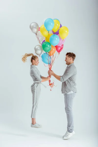 Couple looking at each other and jumping with bundle of colorful balloons on grey background — Stock Photo