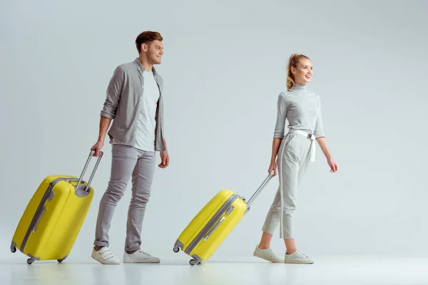 Sonriente pareja llevando maletas amarillas sobre fondo gris, concepto de viaje - foto de stock