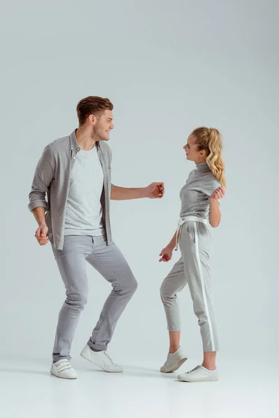 Belo casal em roupas cinza olhando um para o outro e dançando isolado em cinza — Fotografia de Stock