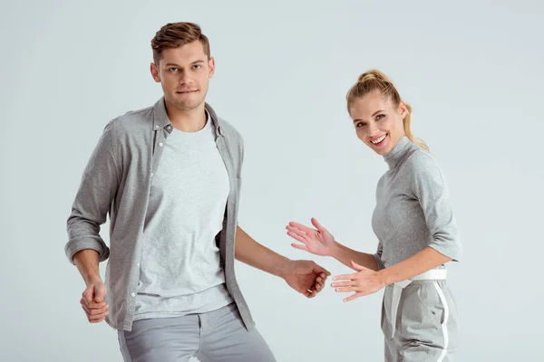 Man dancing while smiling woman looking at camera and making robot moves isolated on grey — Stock Photo