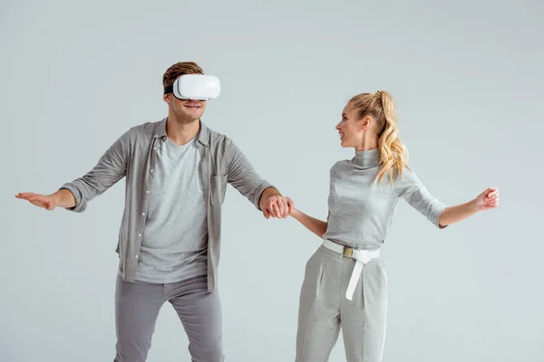 Casal em roupas cinza de mãos dadas, enquanto o homem experimentando realidade virtual isolado em cinza — Fotografia de Stock