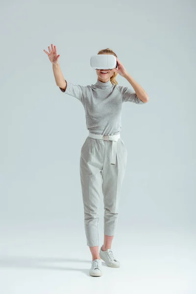 Excited girl in grey clothing gesturing while having virtual reality experience on grey background — Stock Photo