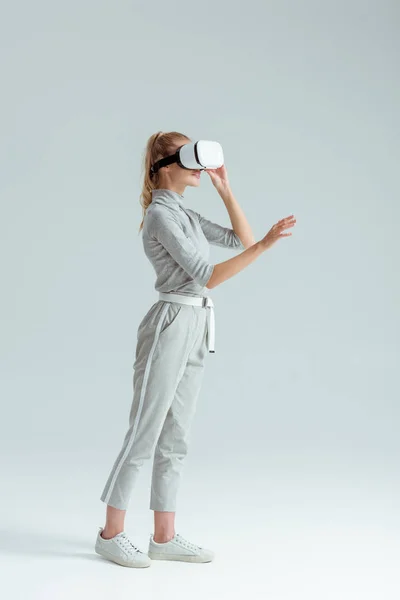 Menina em roupas cinza e vr fone de ouvido gestual, tendo experiência de realidade virtual em fundo cinza — Fotografia de Stock