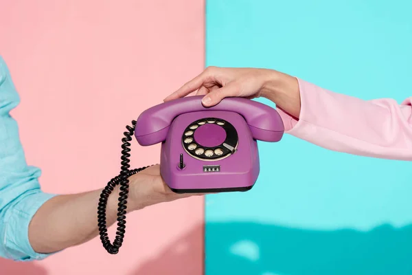 Corte vista de homem e mulher segurando roxo vintage telefone no fundo rosa e azul — Fotografia de Stock