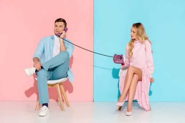 Dissatisfied woman holding purple vintage telephone while man talking with pink and blue background — Stock Photo