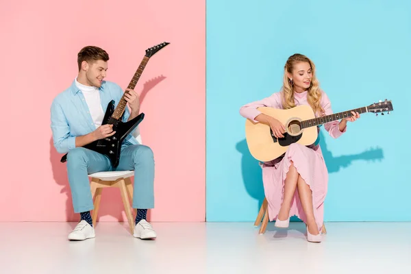 Schönes Paar spielt elektrische und akustische Gitarren auf rosa und blauem Hintergrund — Stockfoto