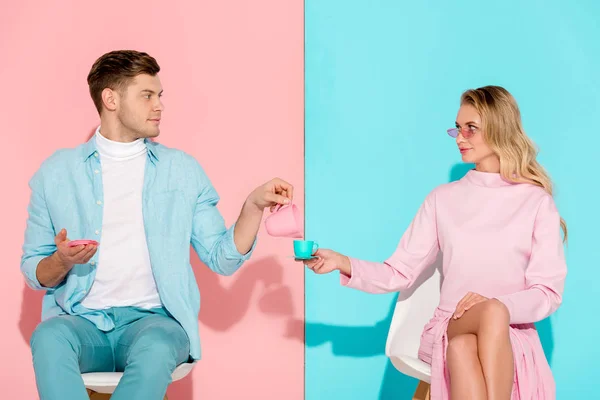 Schöner Mann mit Spielzeugmilchkanne, während Frau mit Kaffeetasse auf rosa und blauem Hintergrund — Stockfoto