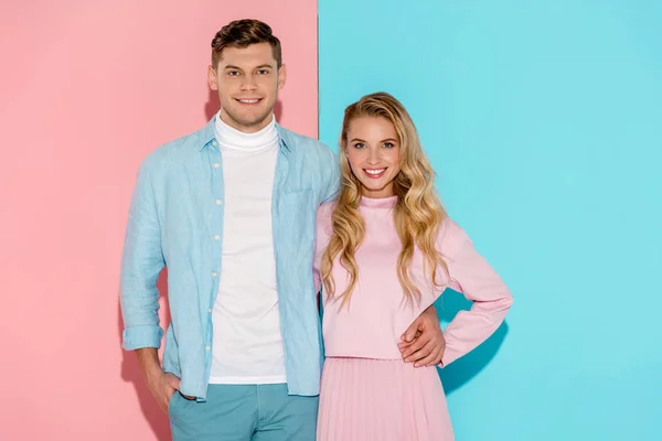 Casal feliz olhando para a câmera e posando no fundo rosa e azul — Fotografia de Stock