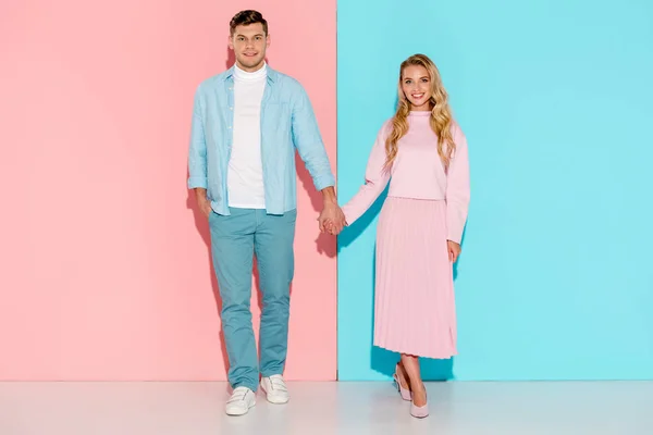 Schönes Paar hält Händchen und schaut in die Kamera auf rosa und blauem Hintergrund — Stockfoto