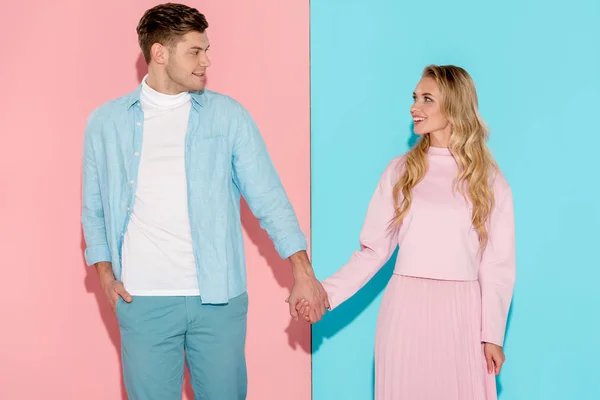 Pareja feliz tomados de la mano y mirándose el uno al otro sobre fondo rosa y azul - foto de stock