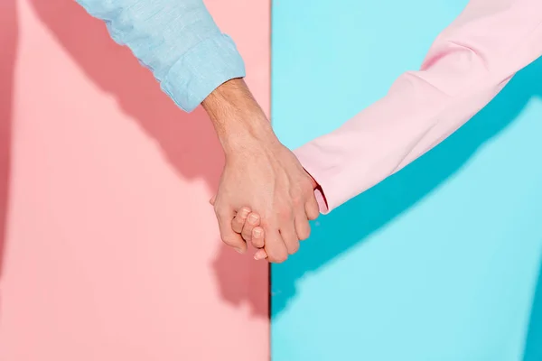 Vista parcial de pareja cogida de la mano sobre fondo rosa y azul - foto de stock