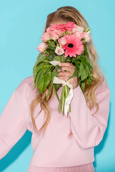 Femme en vêtements roses se cachant derrière un beau bouquet sur fond bleu — Photo de stock