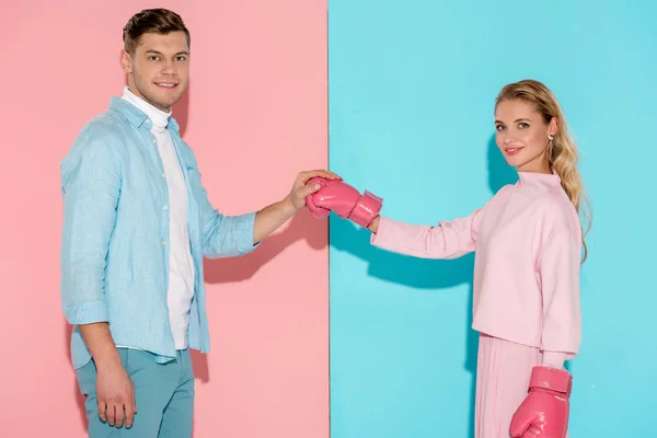 Hombre mirando a la cámara y sosteniendo el guante de boxeo de la mujer sobre fondo rosa y azul - foto de stock
