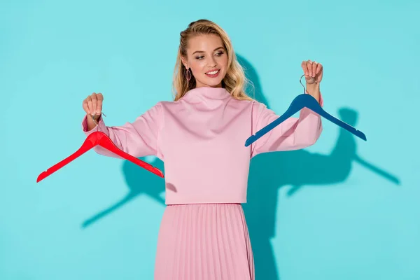 Beautiful woman holding empty clothes hangers on turquoise background — Stock Photo