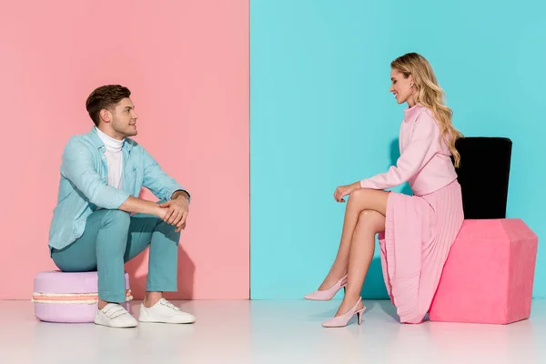 Couple assis sur de grands modèles de macarons et vernis à ongles sur fond rose et bleu — Photo de stock