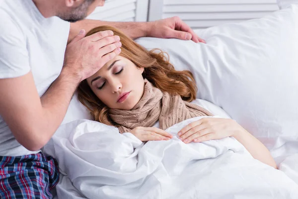Marido tocando la frente de la esposa enferma con fiebre en la cama - foto de stock