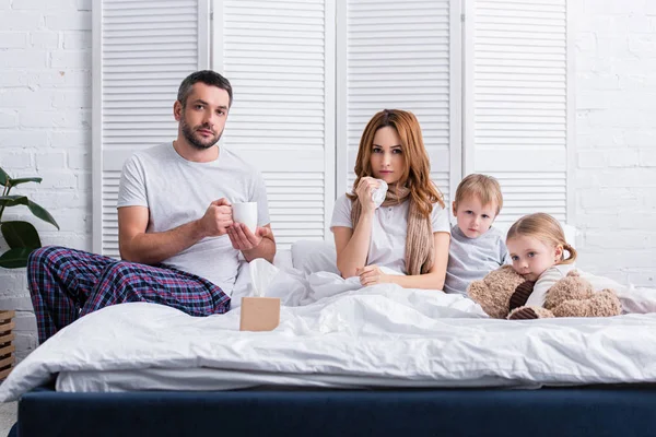 Marido e hijos apoyando a la madre enferma en el dormitorio, mirando a la cámara - foto de stock