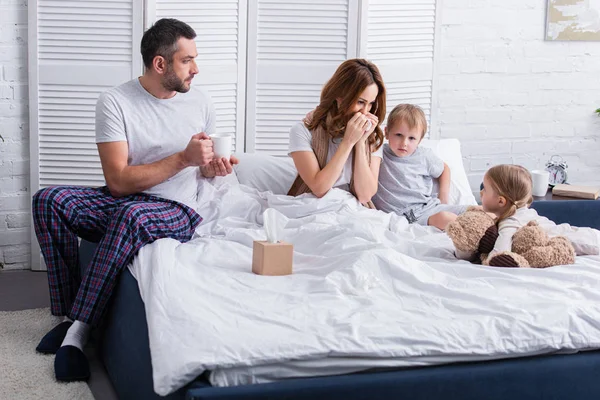 Kinder unterstützen kranke Mutter im Schlafzimmer, Ehemann hält Tasse Tee — Stockfoto