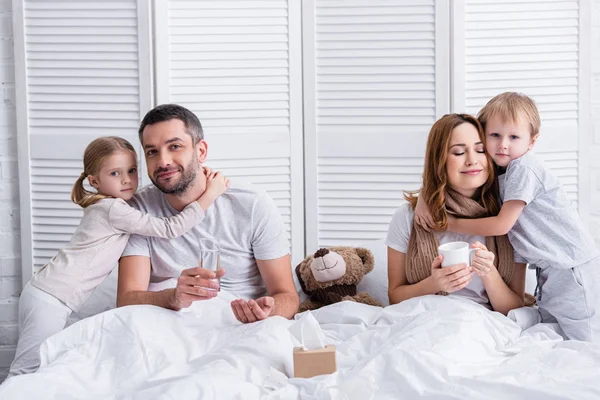 Adorables niños abrazando a los padres enfermos en el dormitorio - foto de stock