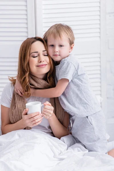 Entzückender Sohn umarmt kranke Mutter im Schlafzimmer — Stockfoto