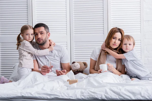 Entzückende Kinder umarmen kranke Mutter und Vater im Schlafzimmer und schauen in die Kamera — Stockfoto