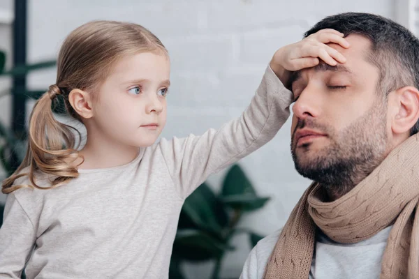 Portrait of adorable daughter touching sick father forehead and checking temperature in bedroom — Stock Photo
