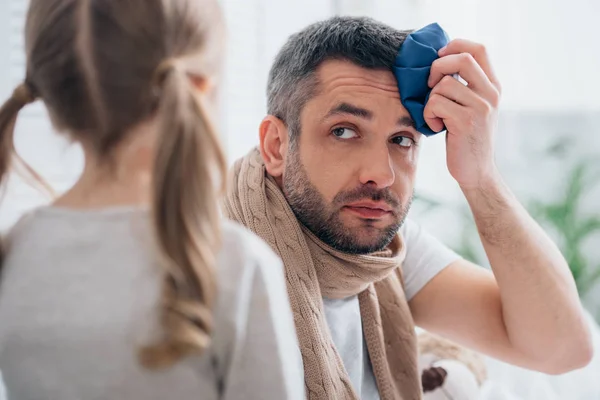Daughter looking at sick father touching head with ice pack in bedroom — Stock Photo