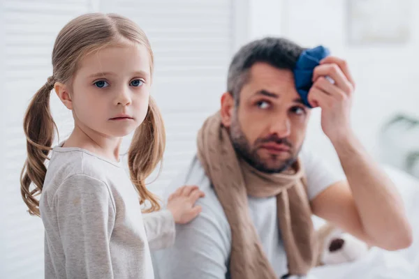 Daughter supporting sick father touching head with ice pack in bedroom — Stock Photo