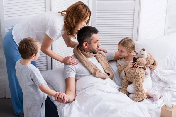 Высокий угол зрения жены и детей, заботящихся о больном отце в спальне — стоковое фото