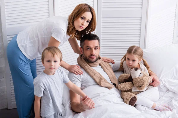 Moglie e figli prendersi cura del padre malato in camera da letto, guardando la fotocamera — Foto stock